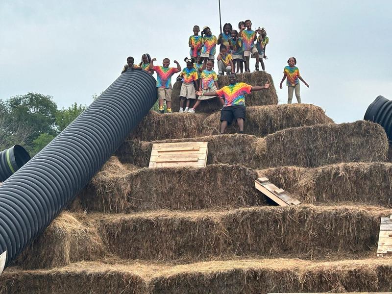 Scholars on top of a large pile of haybales