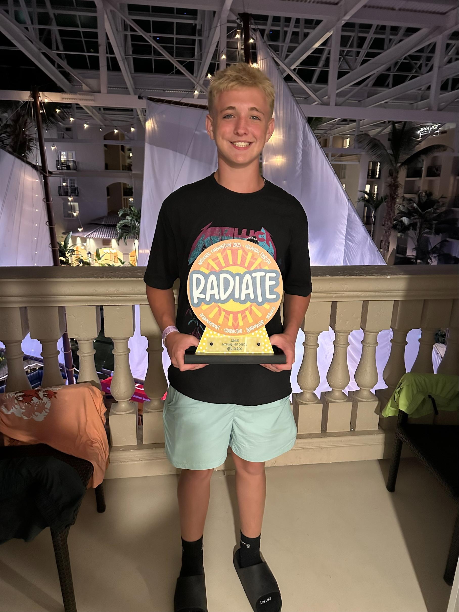 Boy holding Radiate trophy in front of stage area and bright lights. 