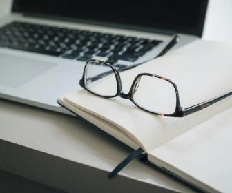 a laptop computer and an open book with a pair of glasses resting on top