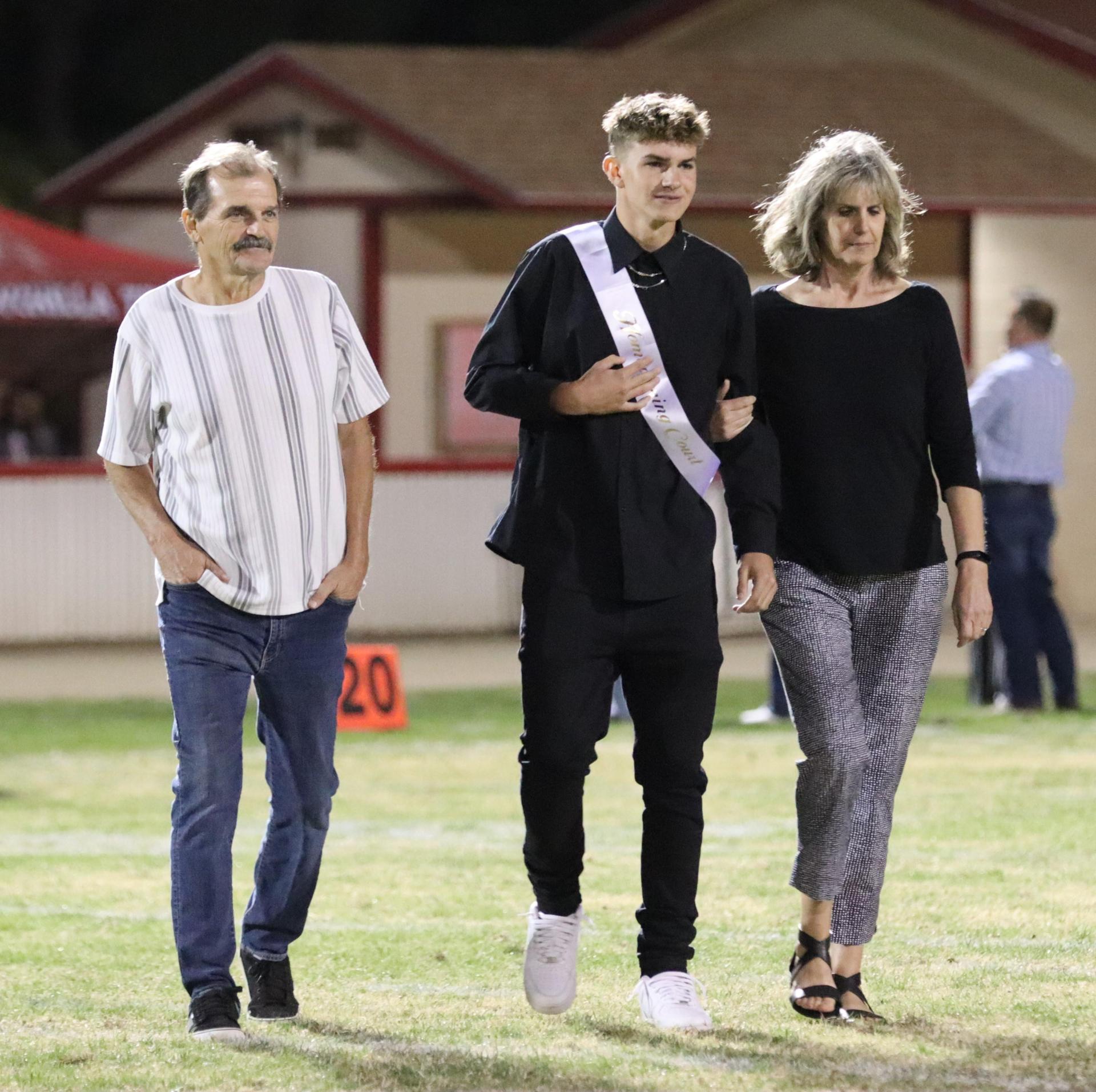 homecoming king and queen candidates walking across the field with their escorts