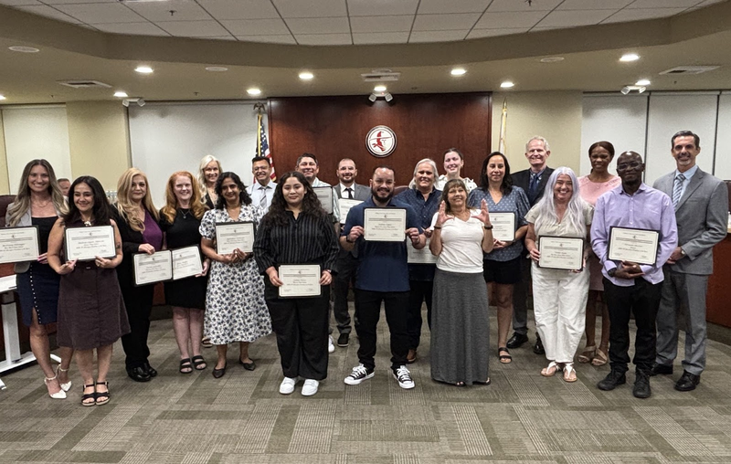 A group of people pose in a board room holding certificates.