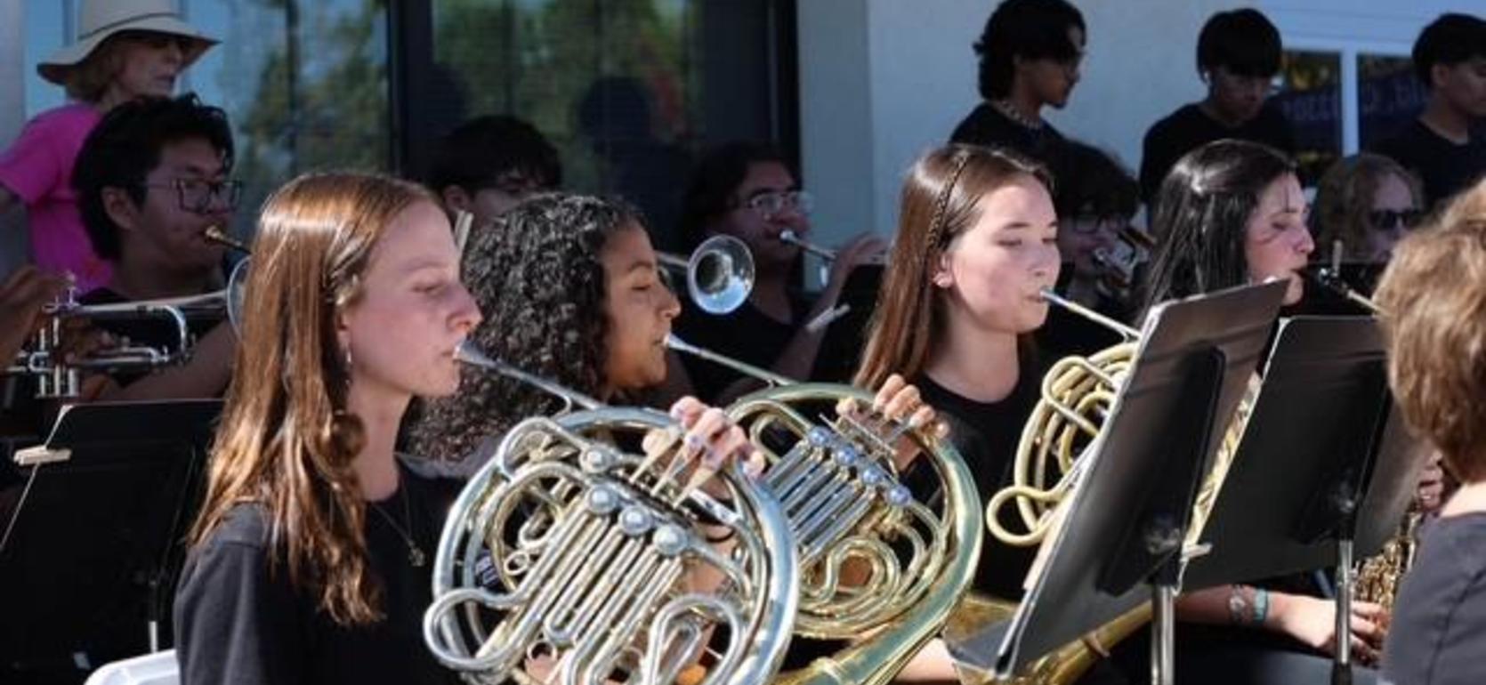 Musicians playing french horns in a band setting, focused on their instruments.