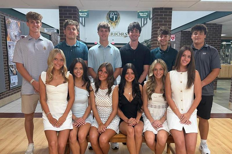 A group of twelve students sit and stand in the high school entryway