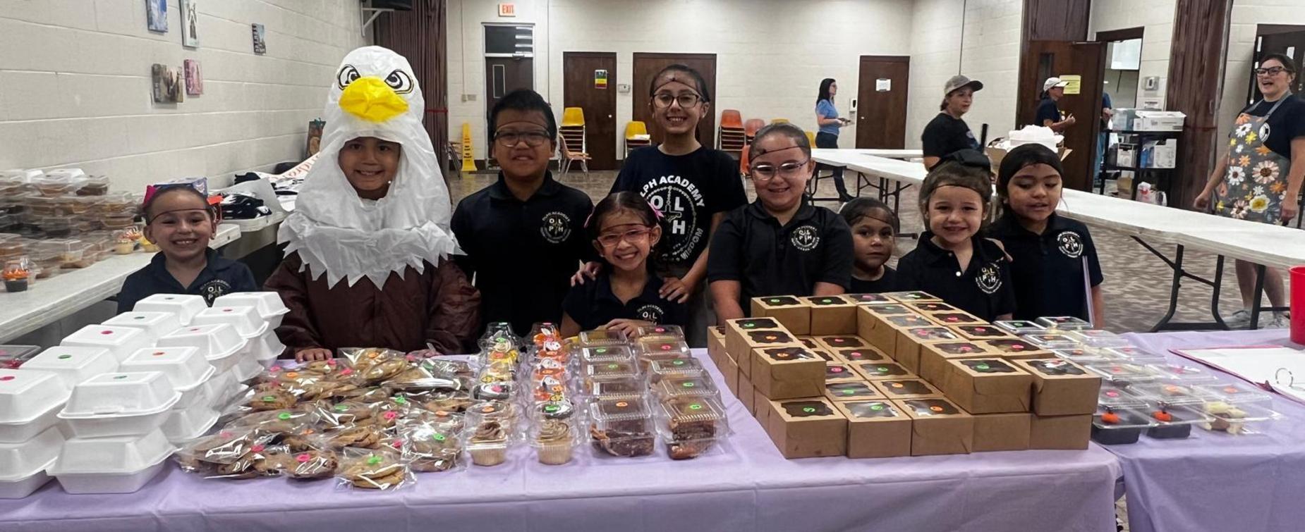 Group of children at a bake sale with various baked goods.