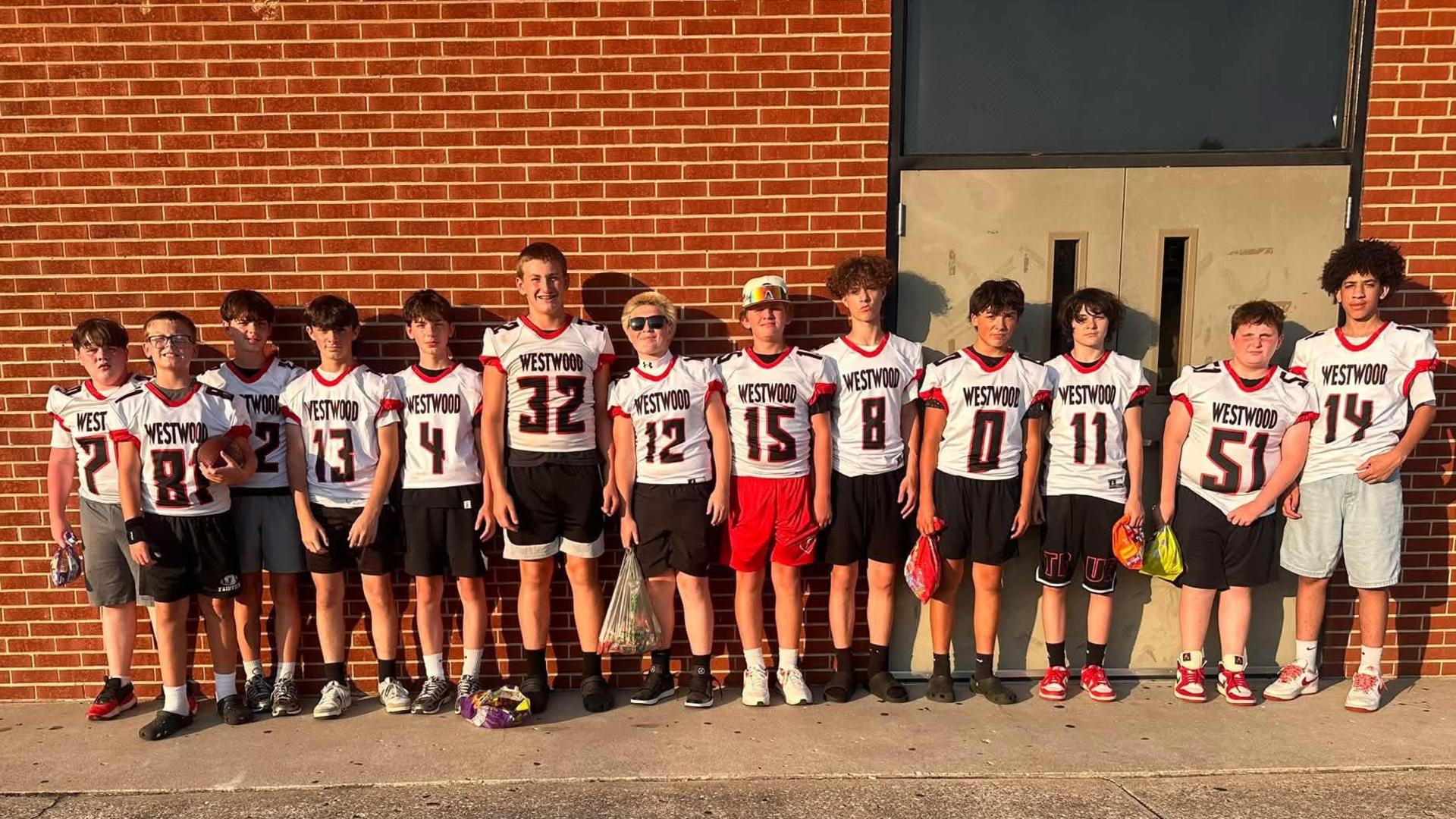 Group of boys in football jerseys standing in front of a brick wall.