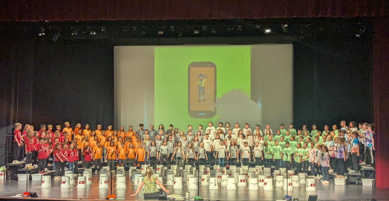 Students performing on stage with colorful shirts and buckets in front.
