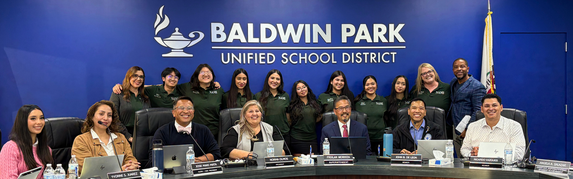 A school board meeting with members and students seated at a large table.