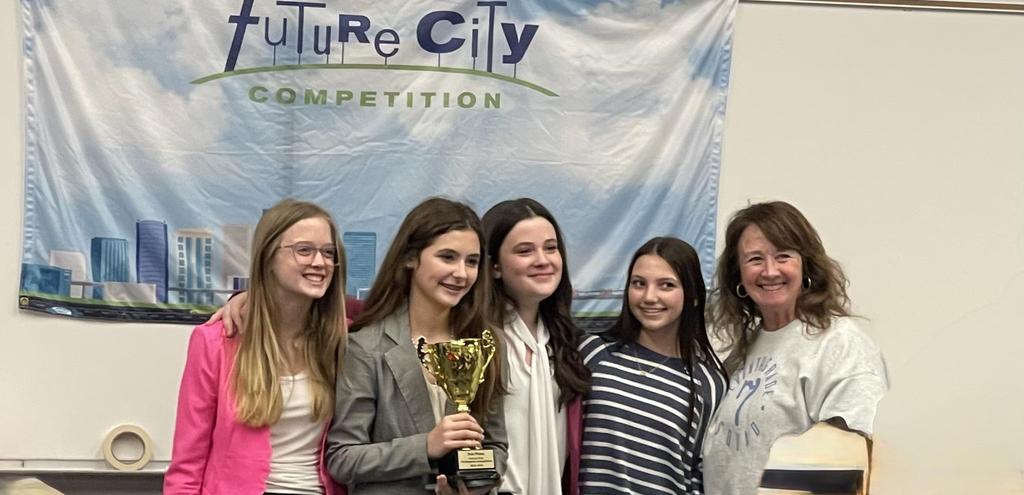 4 young ladies holding up a trophy in front of a banner that reads 'Future City Competition'