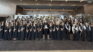 A band in concert uniform smiling with a trophy in an auditorium lobby