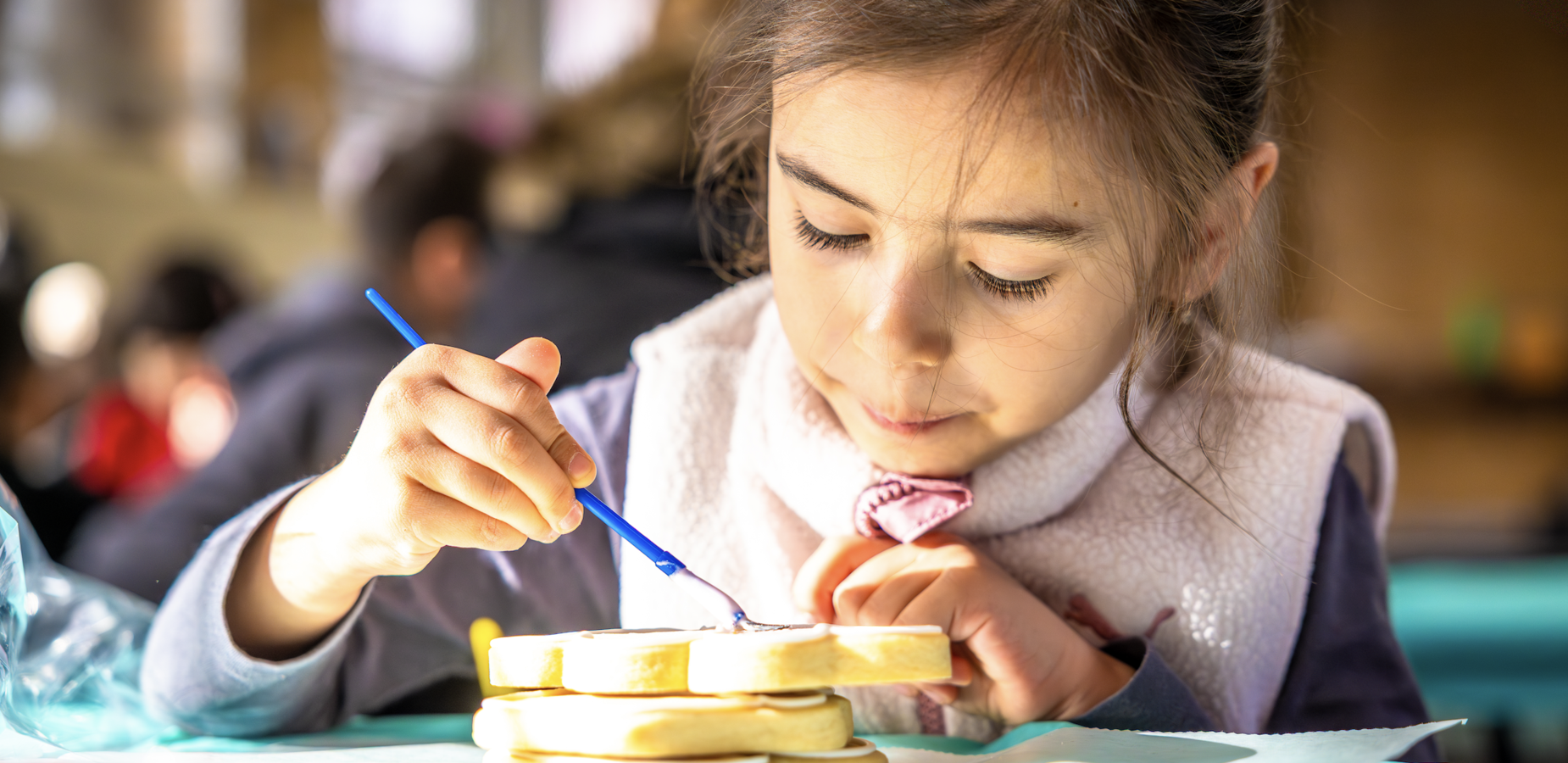 Child concentrating while spreading frosting on sandwich slices.