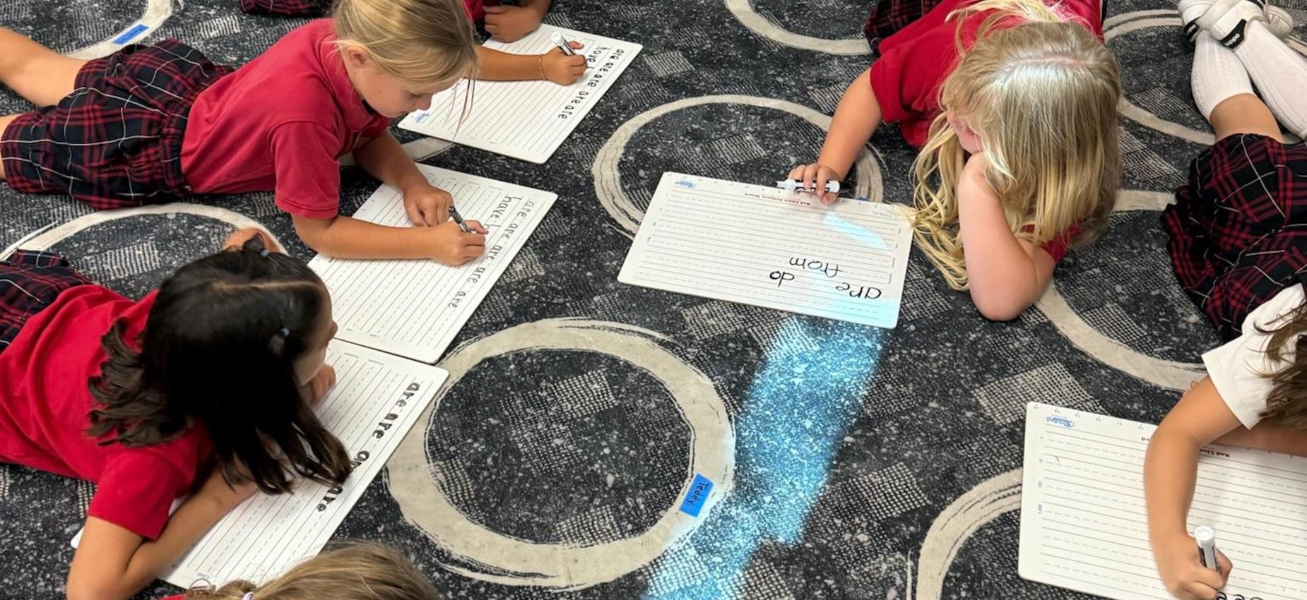 1st grade studnets sit on rug in classroom practicing their sight words on a whiteboard