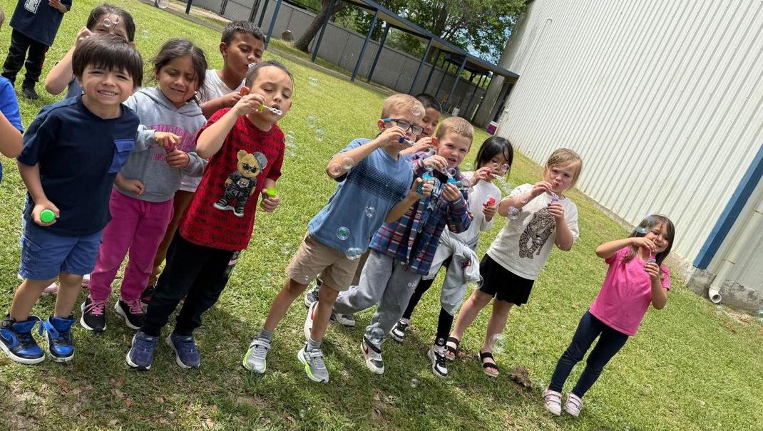 Group of children blowing bubbles outdoors on grass.