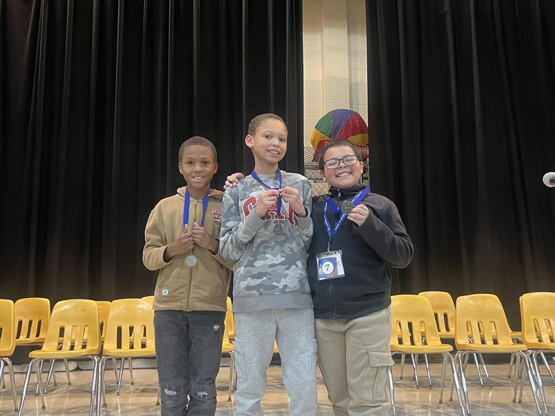 Three children pose with medals on stage.