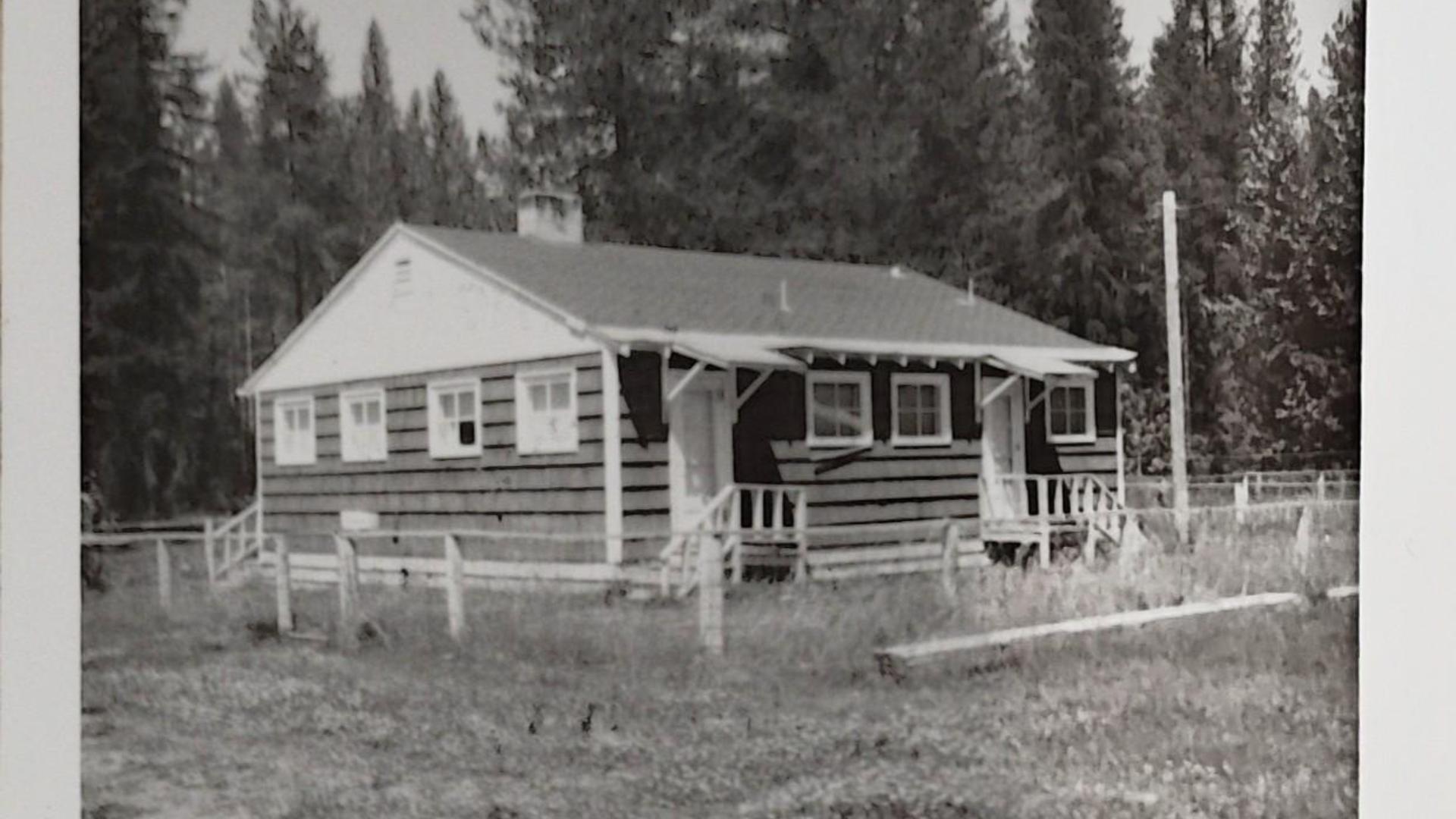 Another view of the wooden cabin with porch, trees in the background.