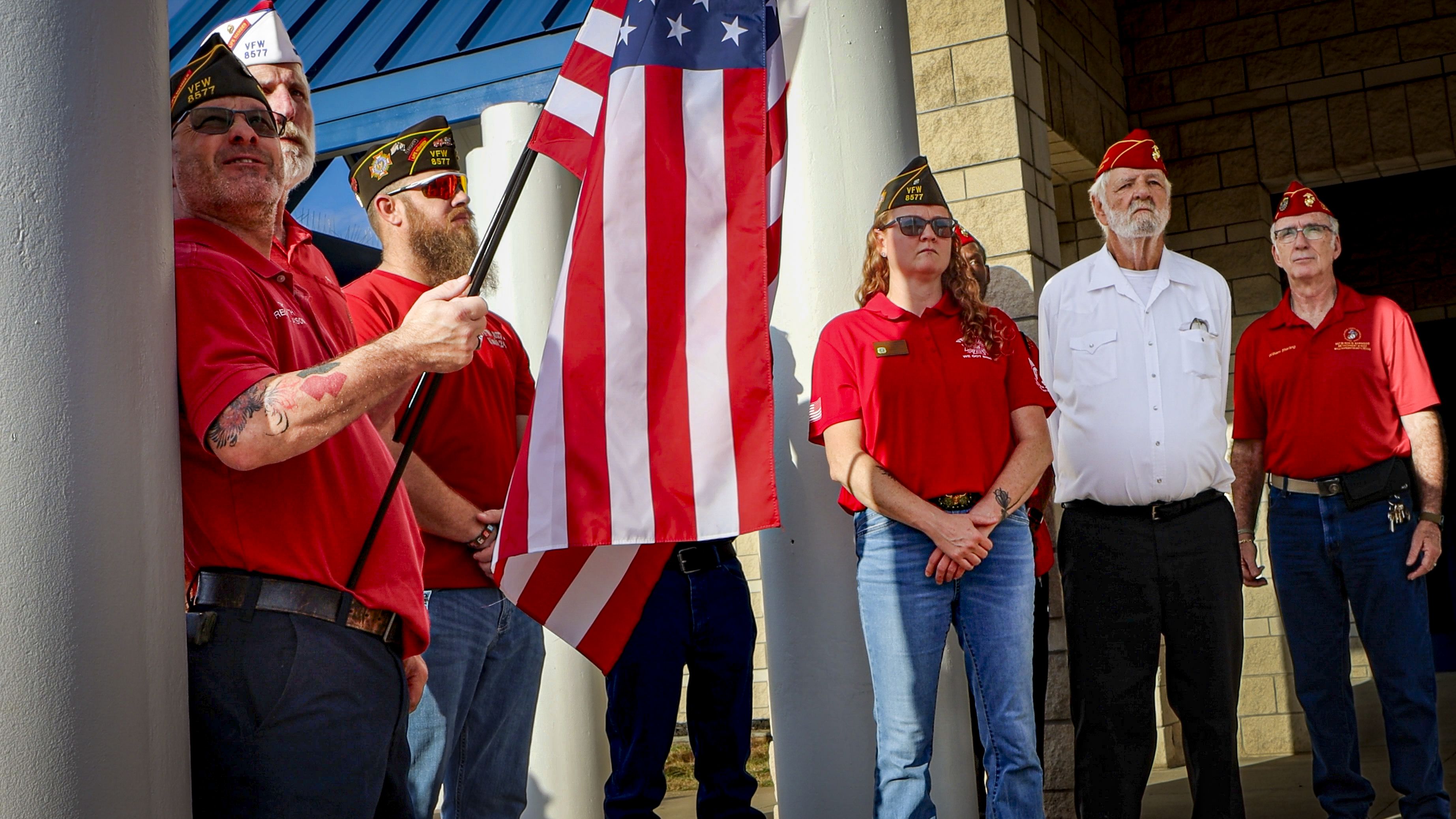Men in VFW polos and hats with one holding American flag