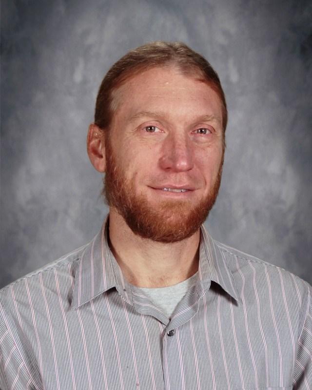 Middle-aged man with a beard in a striped shirt, smiling at the camera.