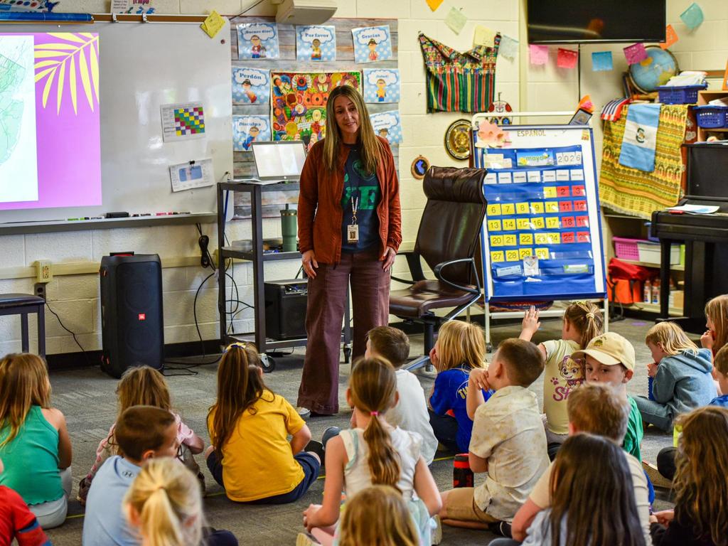A teacher standing at the front of the classroom with students seated on the floor in front of her.