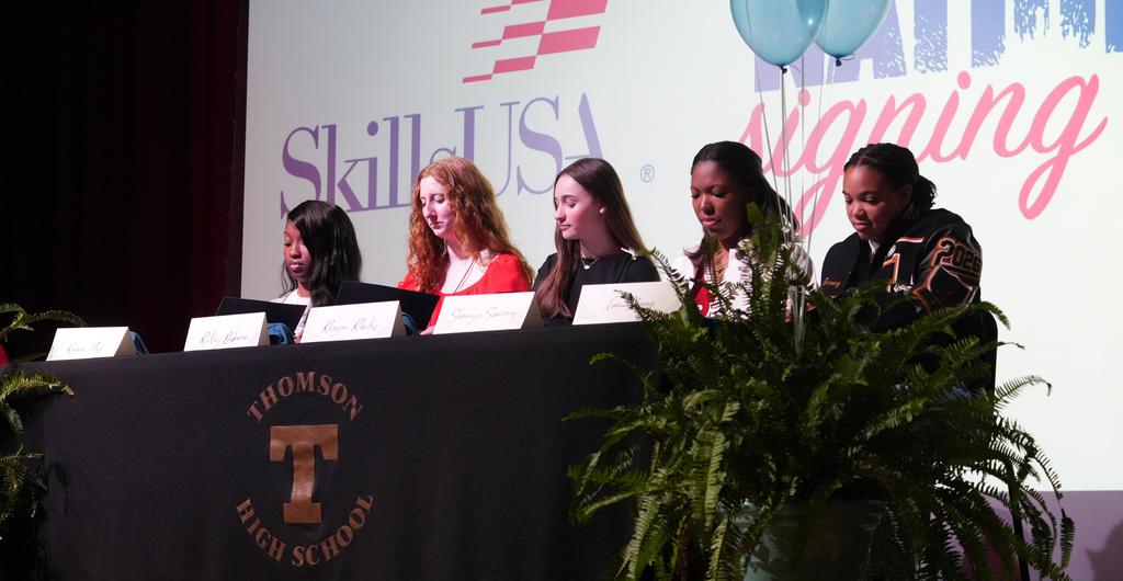 Five students sign commitment letters at a ceremony.