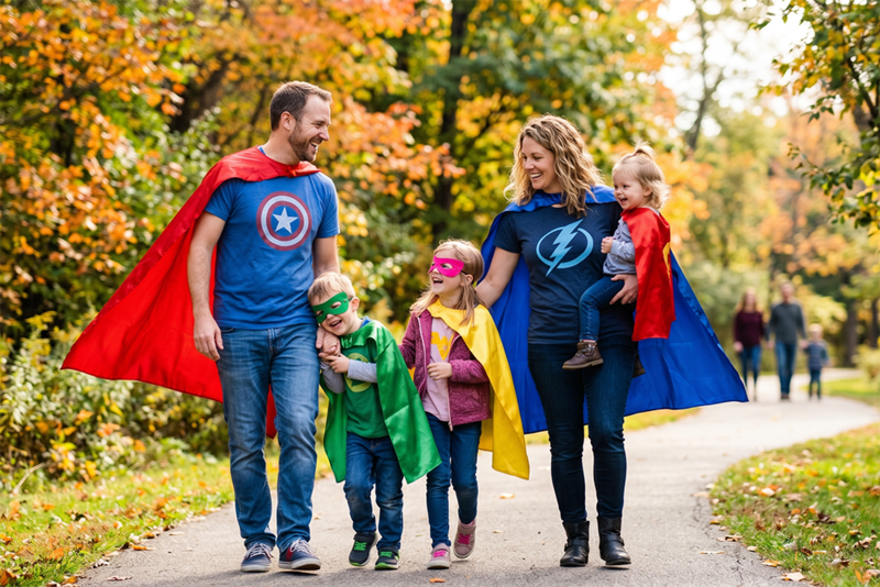 A family in superhero costumes walking down a park path autumn
