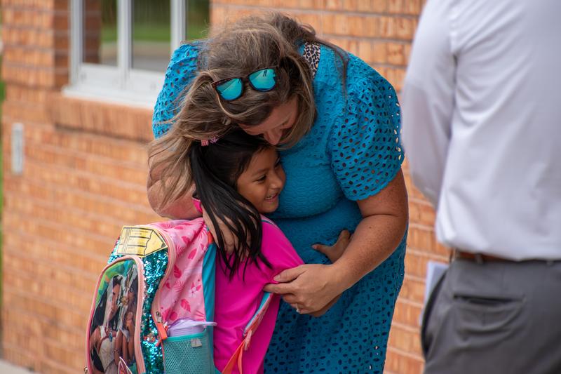 A women hugs a student as they arrive at school.