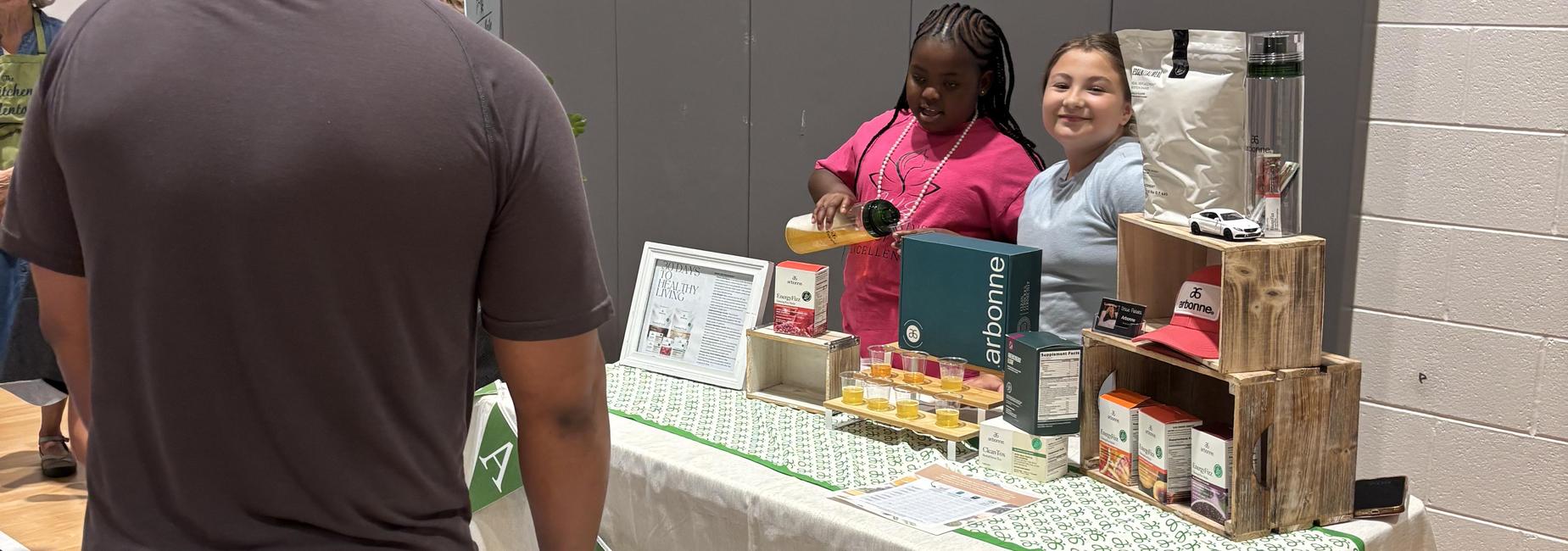 Two smiling children at a table displaying products and informational materials.