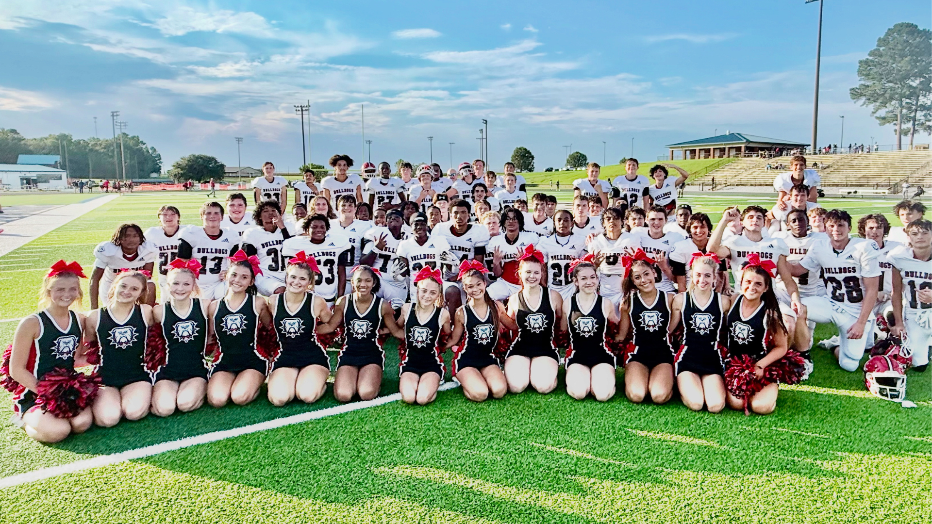 Cheerleaders and football players pose together on the field after a game.