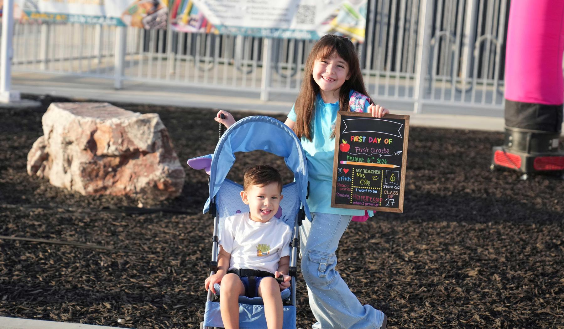 boy in stroller and sister holding a first day of school sign