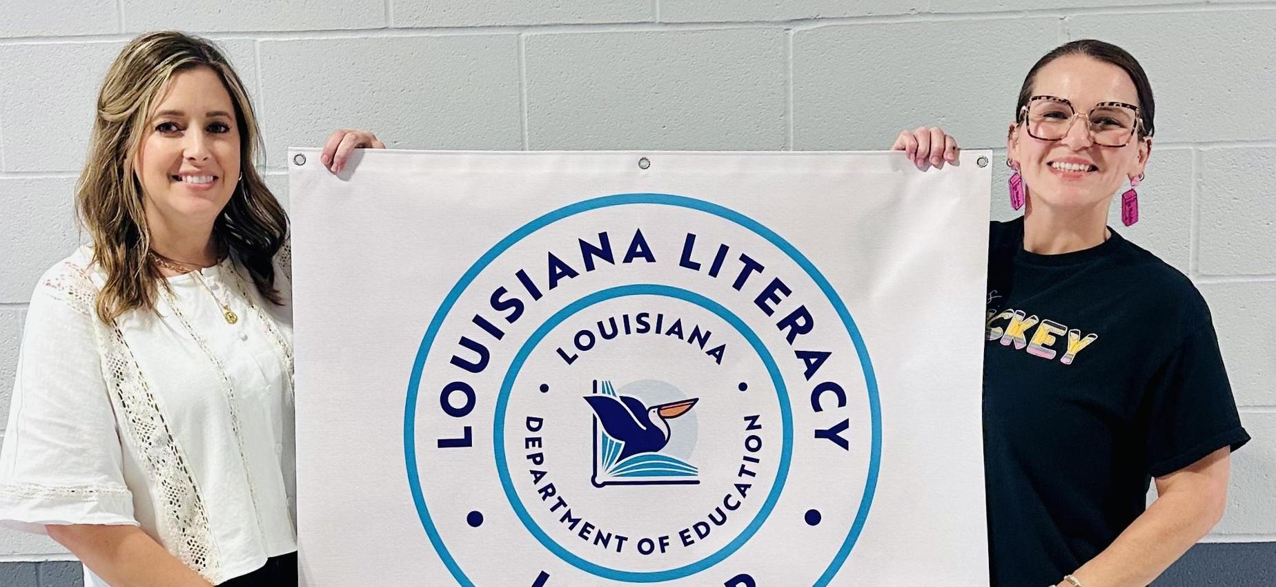 Two women holding a banner recognizing literacy achievement in Louisiana.