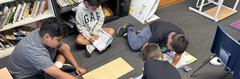 Four children working on projects on the floor with materials and worksheets around them.