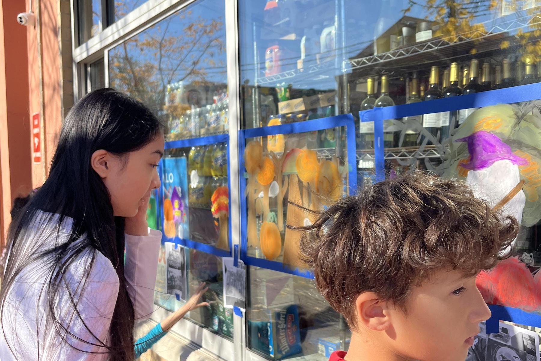 Two children closely observing colorful paintings on a shop window.