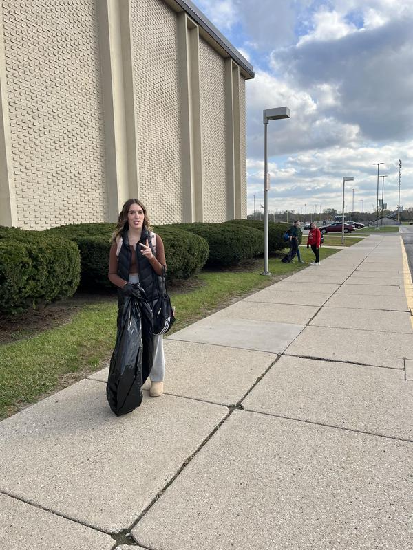 A girl holding a large garbage bag near a building while others walk in the background.