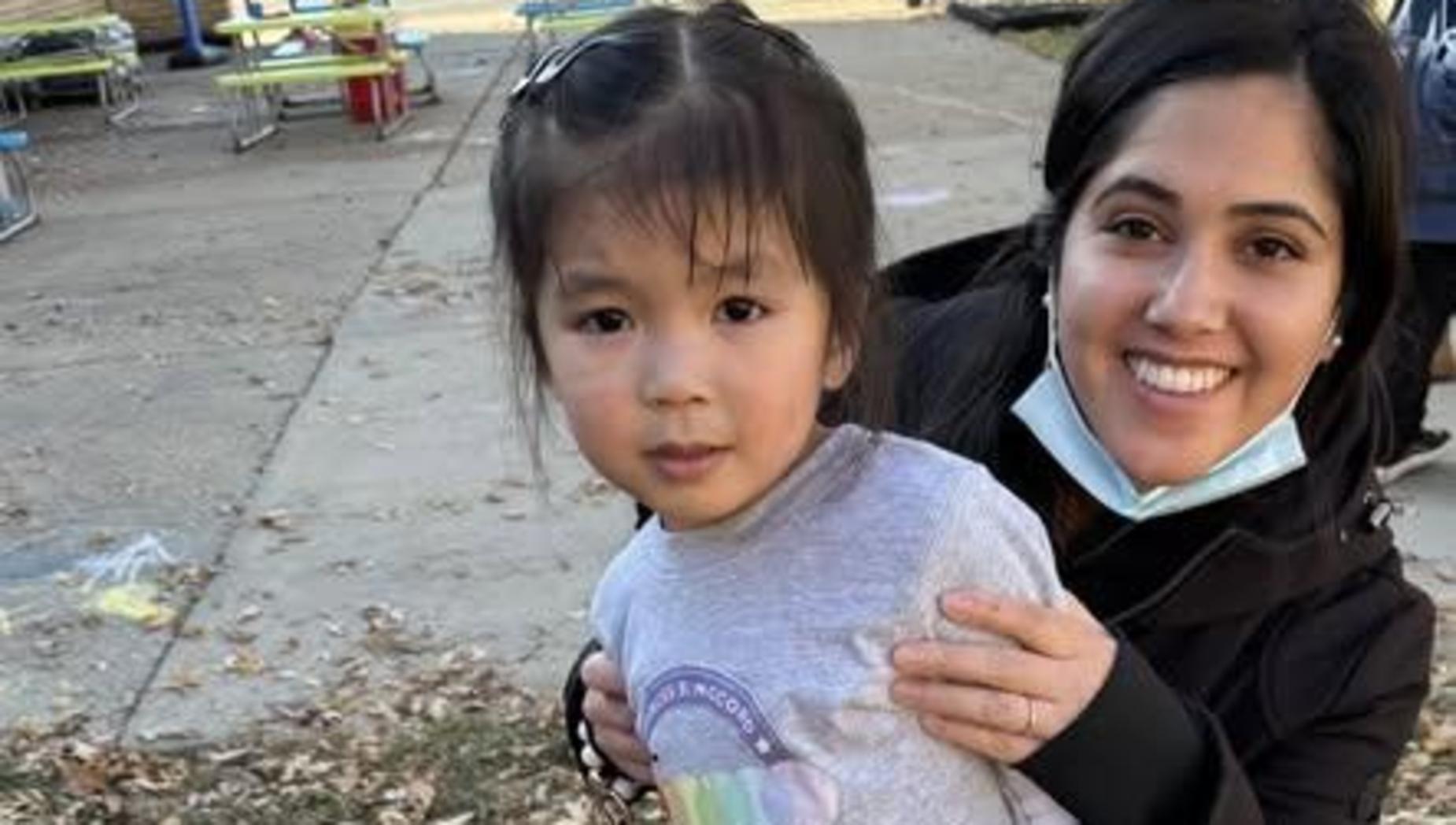 Adult holds a child who is smiling, both surrounded by autumn leaves.