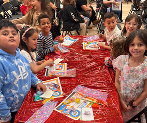2nd grade students gathered around a red table-clothed table with books