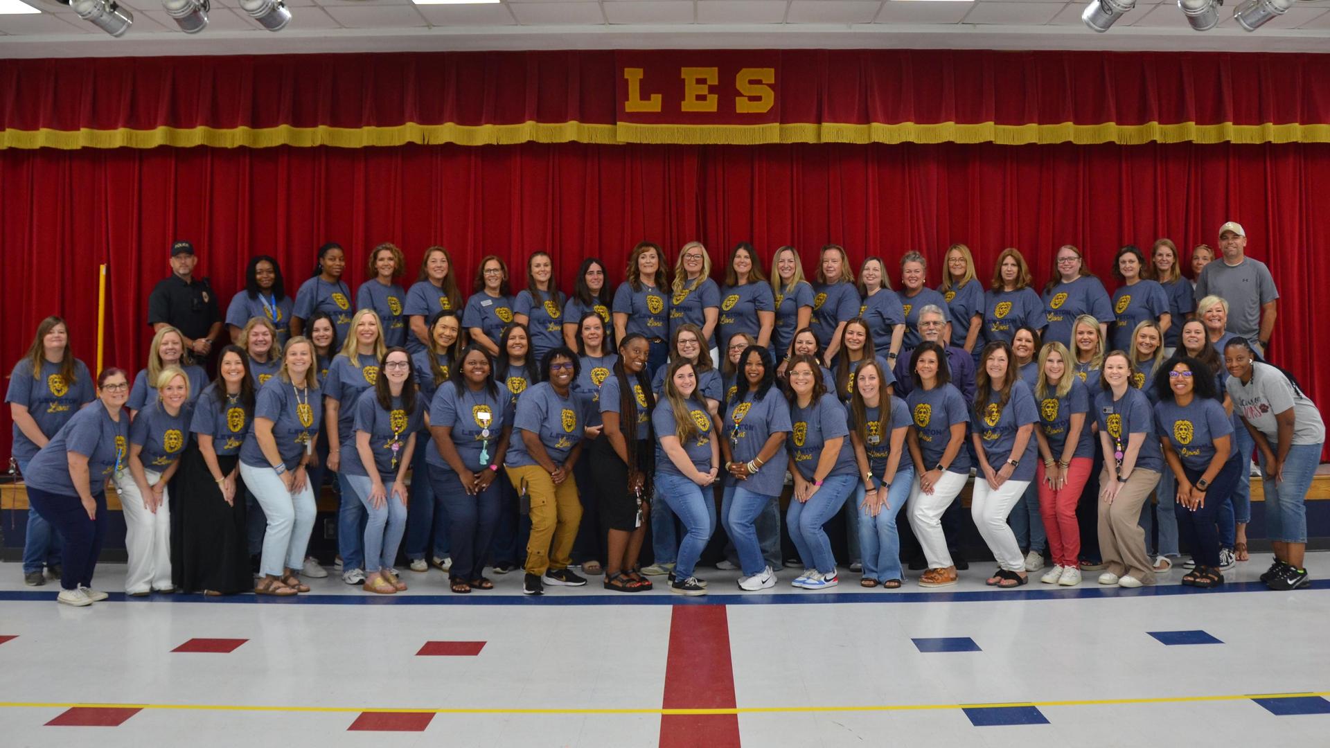 Group of educators and staff posing together in a school auditorium.