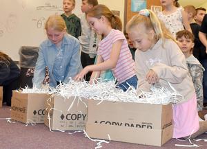 Children playing with shredded paper in cardboard boxes during an activity.