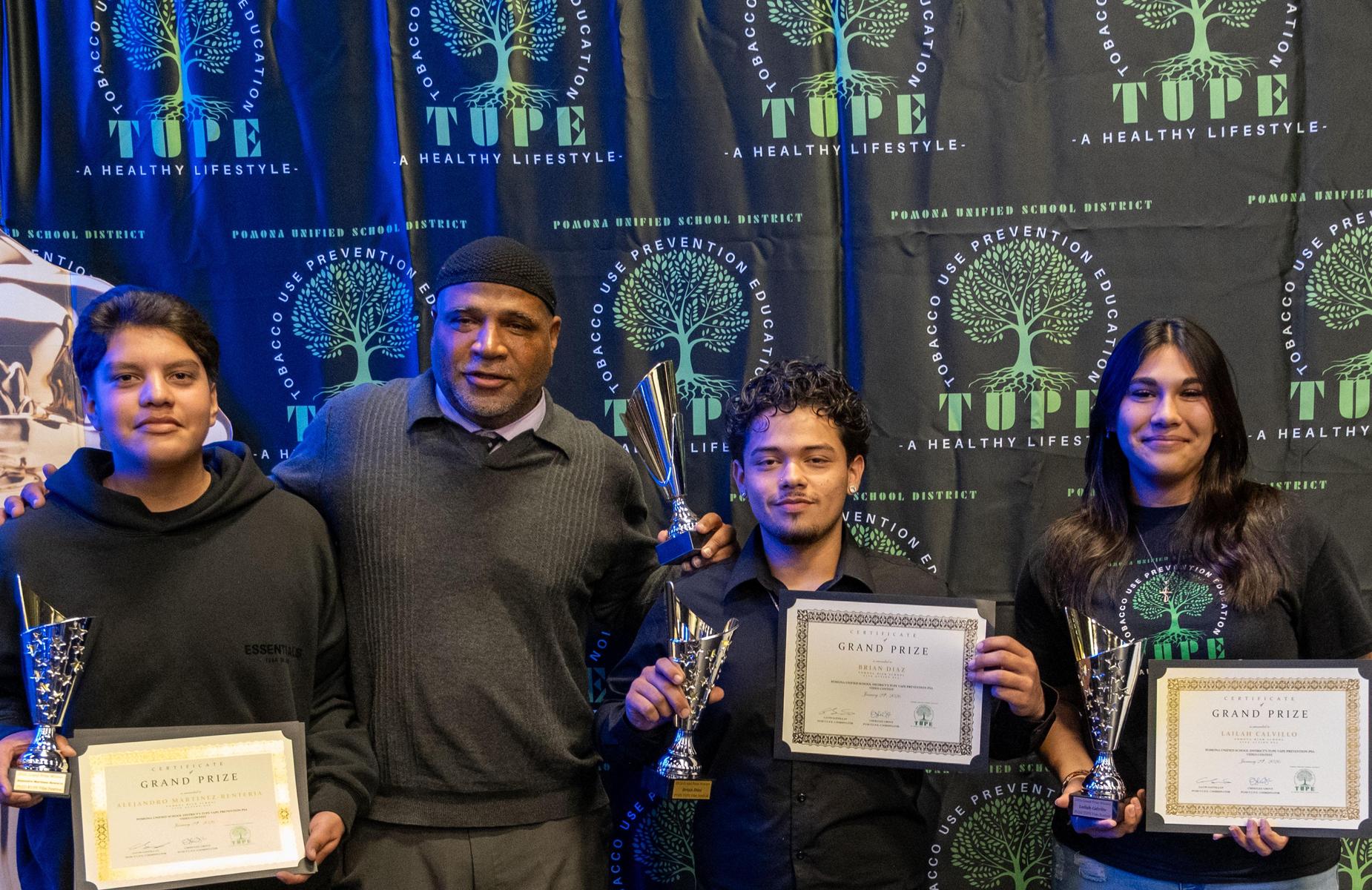 four persons holding certificates and awards