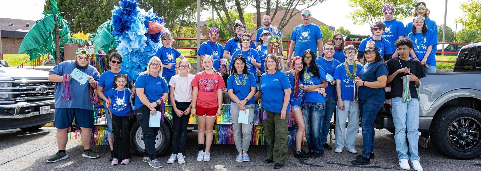 Large group of people posing in decorated attire on a parade float with colorful decorations.