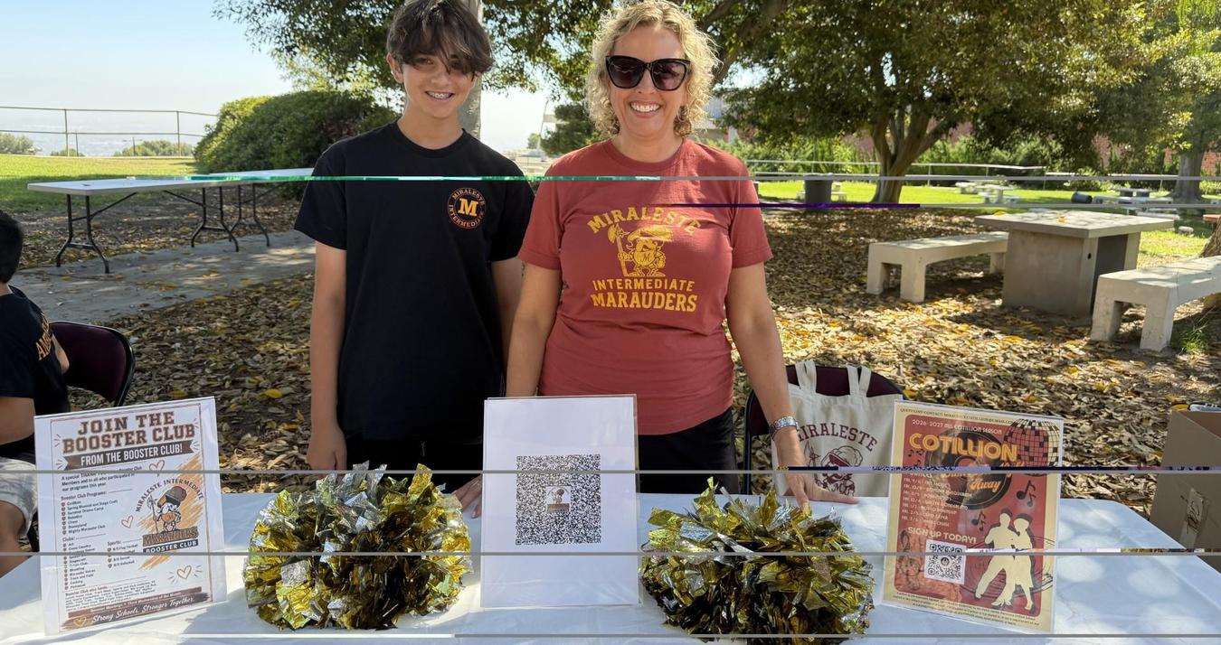 A woman and a boy stand behind a table displaying school materials.