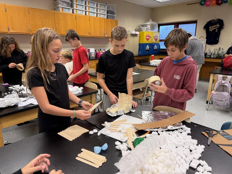students gathered around table filled with supplies building a nest