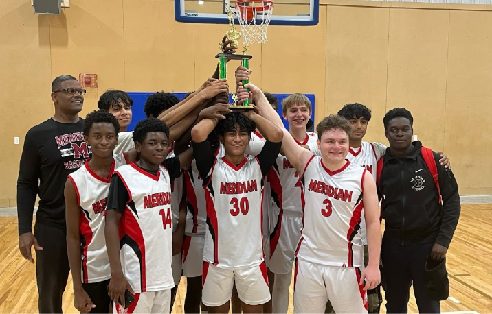 Students stand in front of a basketball net holding up a trophy, with coach on the left