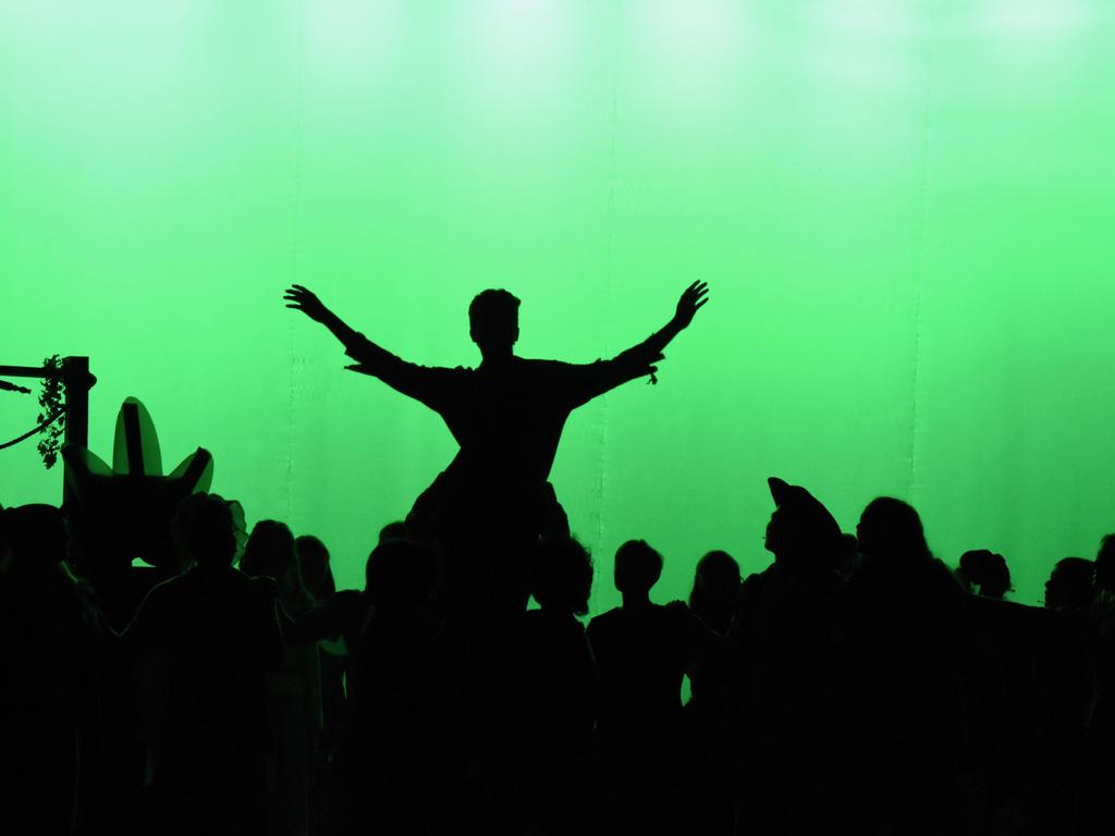 A person with both arms out, held on the shoulders of others, in silhouette against a green background.