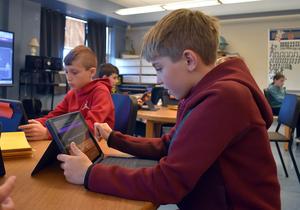 Boys using tablets for learning at a table in a classroom.