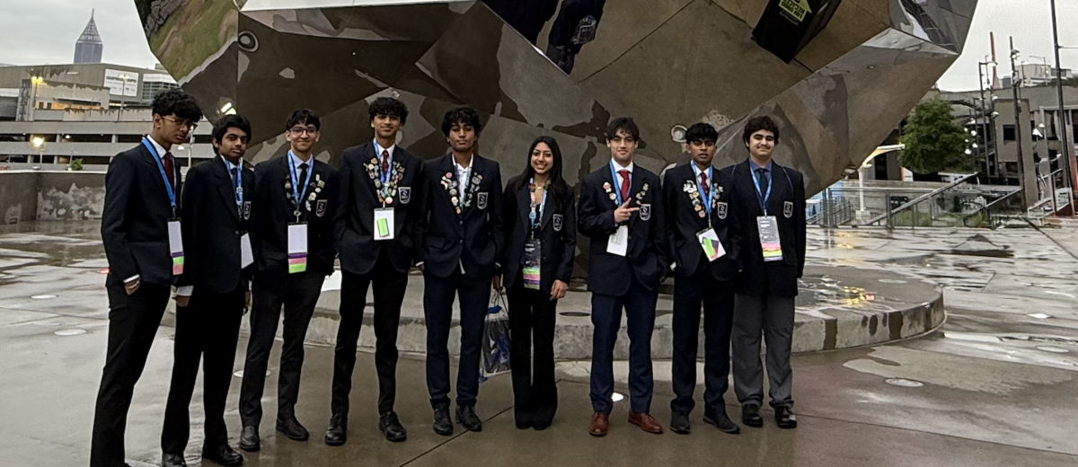 Students in suits stand in front of reflective mirror installation