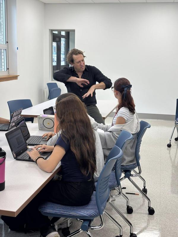 Author James sitting on a desk speaking with 3 students