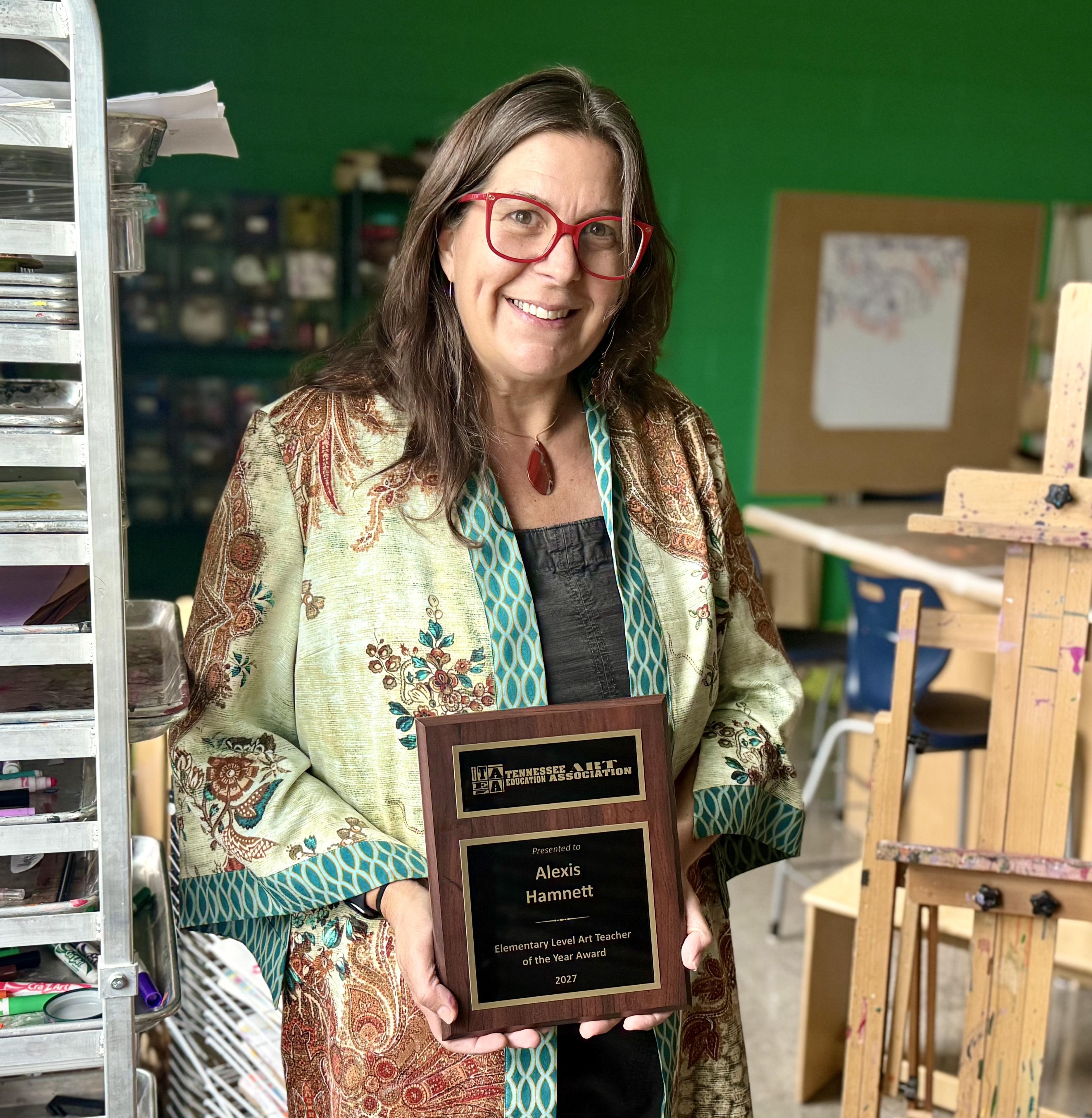 Smiling Lady holding plaque standing in front of art supplies