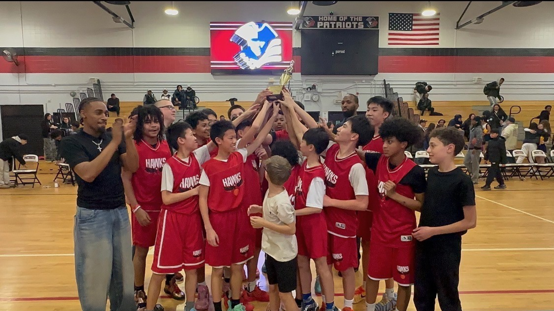 A basketball team celebrates with a trophy in a gymnasium.