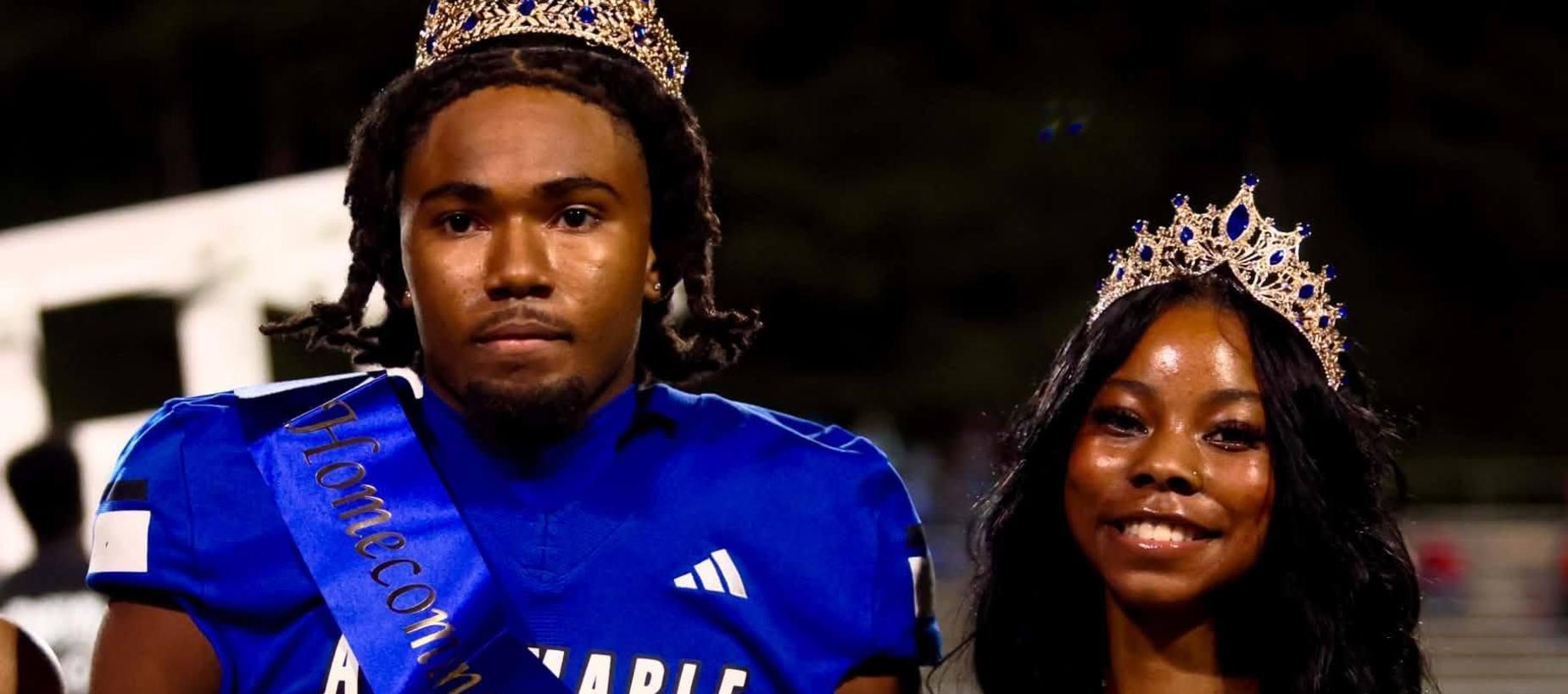 Football players in blue jerseys with a homecoming king and queen celebrating.