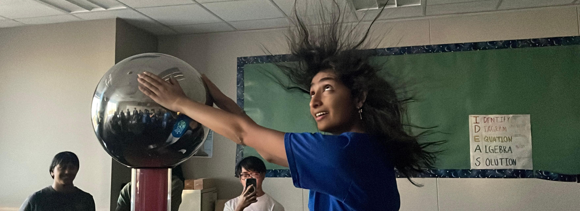 A girl with long hair reacting to an electric current from a science demonstration.