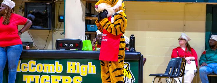 A mascot in a tiger costume stands by a table at McComb High School.