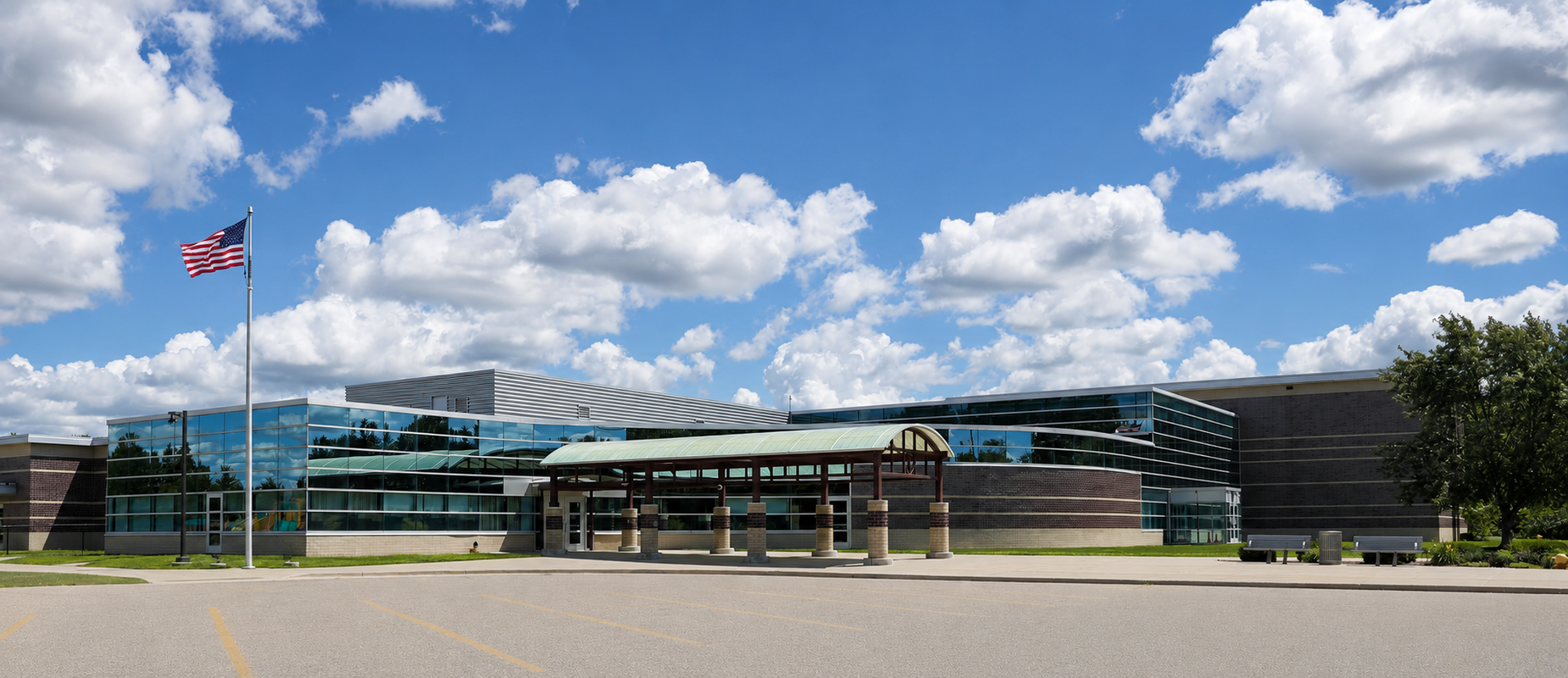 The exterior of Century Park has a flag on the left. This photo is taken on a sunny day, highlighting the glass windows. There is a canopy in the center foreground.